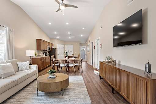 A living room with a white couch, wooden furniture, and a flat screen TV mounted on the wall.