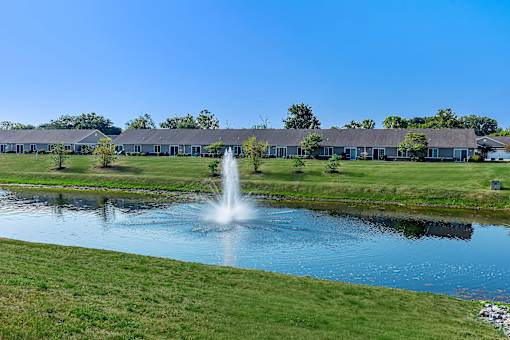 A fountain in the middle of a pond in front of a building.