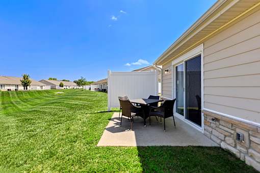 A patio with a table and chairs is in front of a house.
