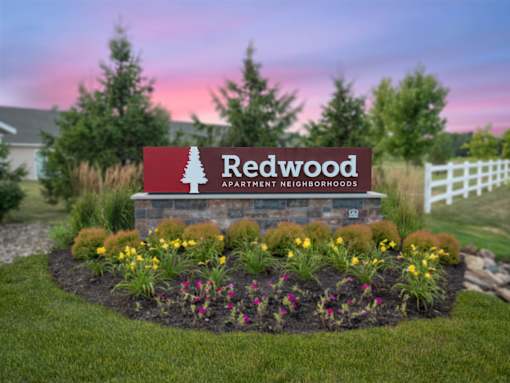 A sign for Redwood Apartment Neighborhoods is surrounded by flowers and greenery.