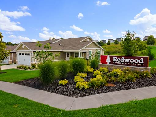 A well-maintained lawn surrounds a house with a sign that reads "Redwood Apartment Neighborhoods.".