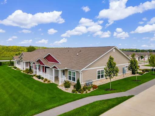 A house with a red roof and a brown roof is surrounded by green grass and trees.