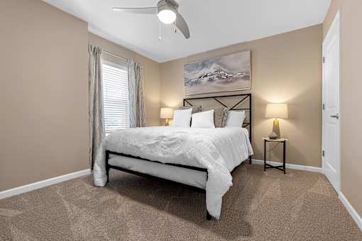 A bedroom with a bed, two lamps, and a painting on the wall.