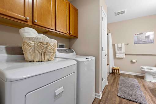 A laundry room with a washer and dryer, a basket of towels, and a bathroom with a toilet in the background.
