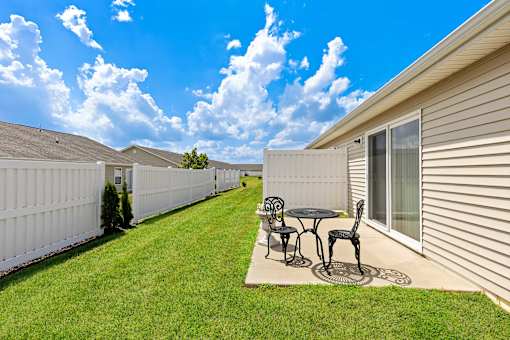 A patio with a table and chairs is surrounded by a white fence.