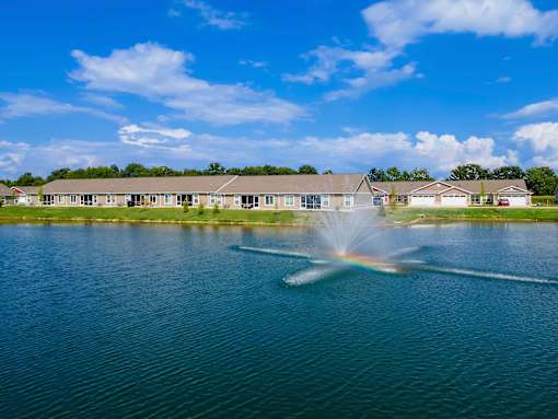 A fountain in the middle of a lake with houses in the background.