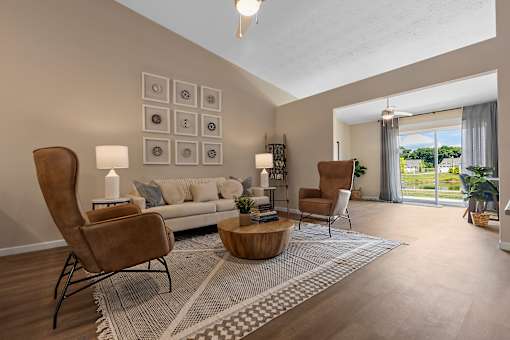 A living room with a grey sofa, a wooden coffee table, and a large window with a view of the outdoors.