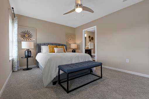 A bedroom with a bed, a bench, and a ceiling fan.