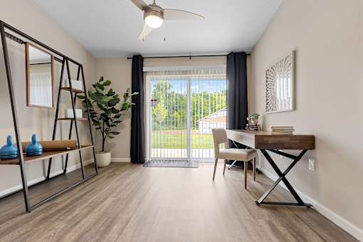 A room with a sliding glass door leading to a backyard, a desk with a chair, and a shelf with decorative items.