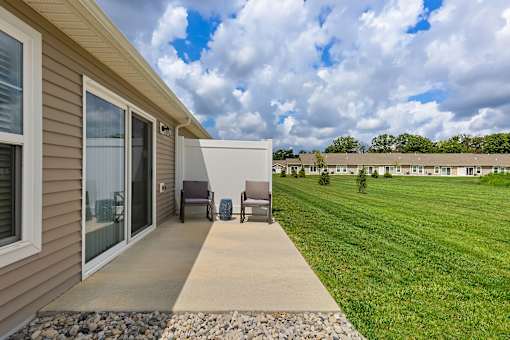 A patio with a chair and a table is in front of a house.