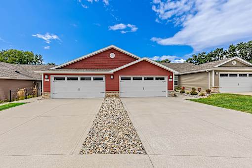 A two-car garage with a red roof and white doors is surrounded by a gravel driveway.