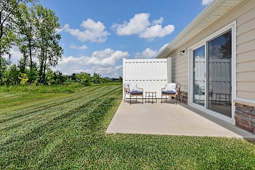 A patio with chairs and a table is on the side of a house.