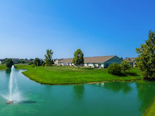 A fountain in the middle of a lake in front of a house.