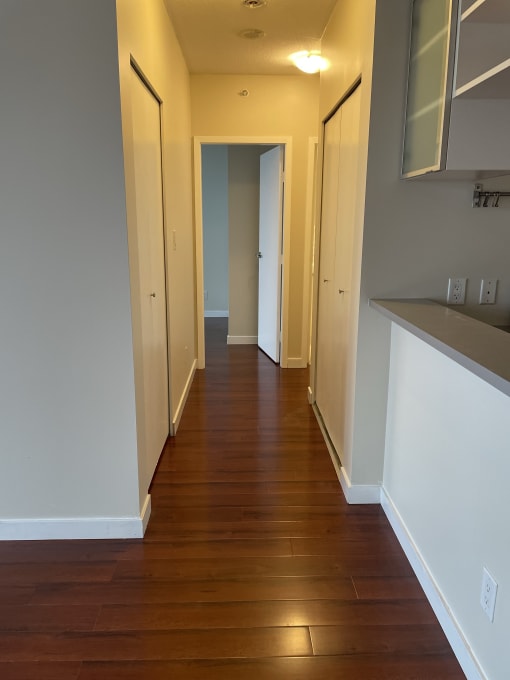 a hallway with wood floors and white walls and a door to a closet