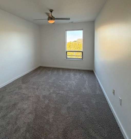 A room with a ceiling fan and a window showing a view of a field.