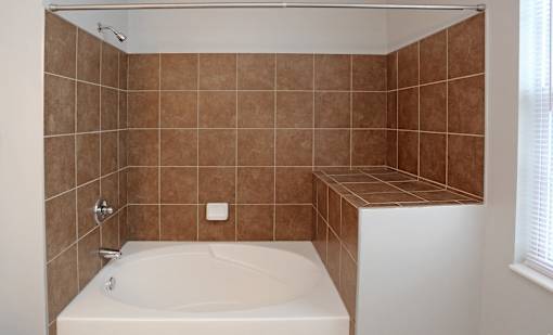 A white bathtub in a bathroom with brown tiled walls.