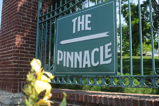 A green sign that says "The Pinnacle" is mounted on a metal fence.