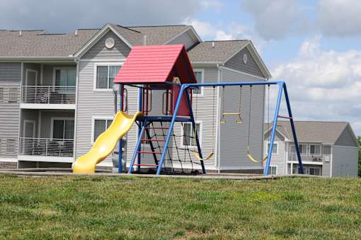 A red and yellow slide in front of a grey house.