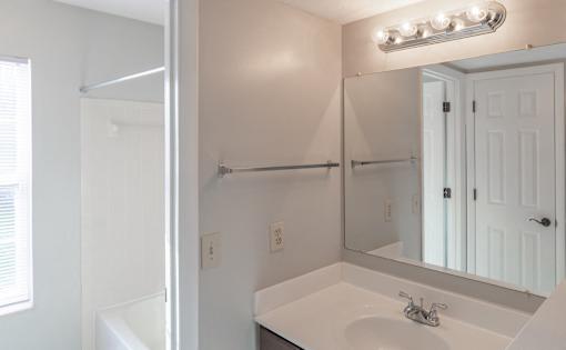 A white bathroom with a sink, mirror, and light fixture.