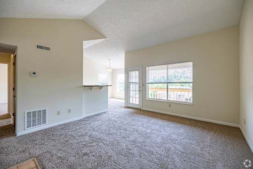 A spacious living room with a carpeted floor and large windows.