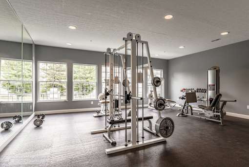 A spacious gym with a variety of equipment including a squat rack, bench press, and dumbbells at Twin Fountains Apartments, Mason, OH