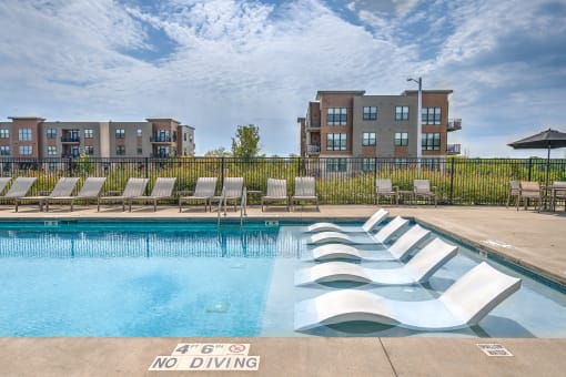 a swimming pool with chaise lounge chairs in front of an apartment building