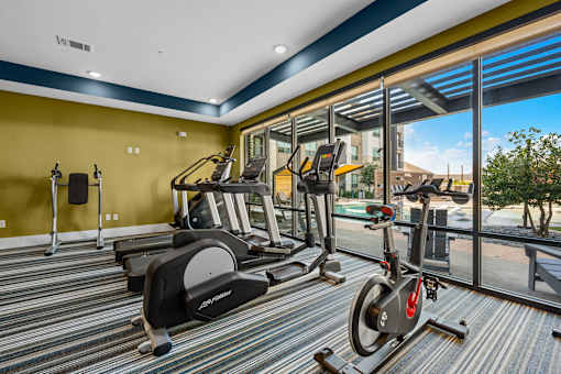 A gym with a yellow wall and a row of treadmills.