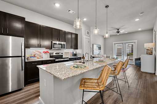 A kitchen with a marble countertop and wooden chairs.
