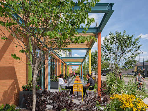 A group of people are sitting at tables under a blue awning.