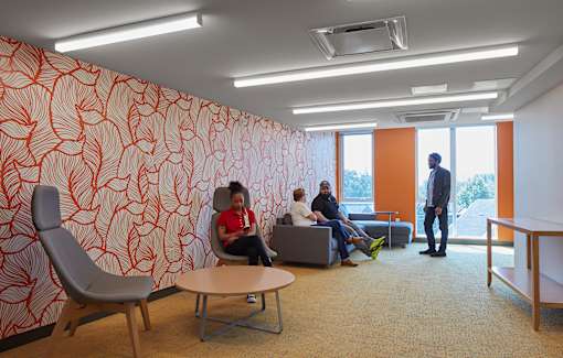 A group of people are sitting in a room with orange wallpaper.