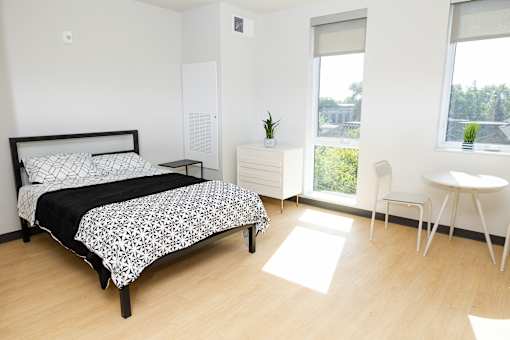 A bedroom with a bed, a nightstand, a chair, and a window.