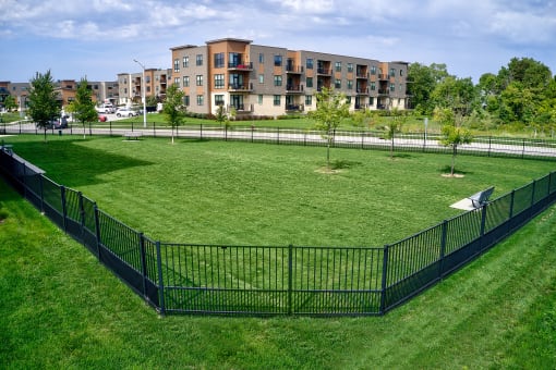 a fenced in dog park with an apartment building in the background