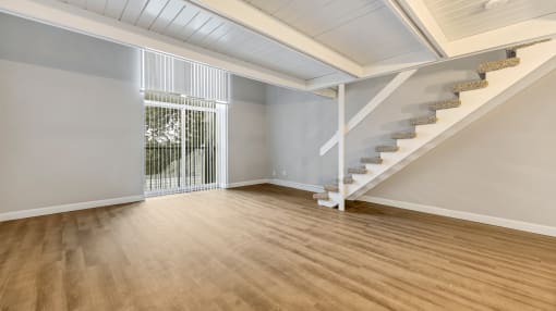 an empty living room with stairs and a door to a balcony