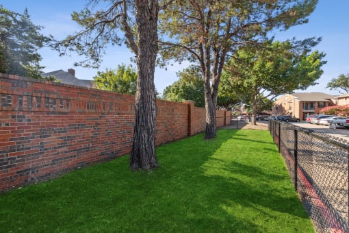 a brick retaining wall with trees and a chain link fence at Wellington at Willow Bend Apartments, Plano, 75093