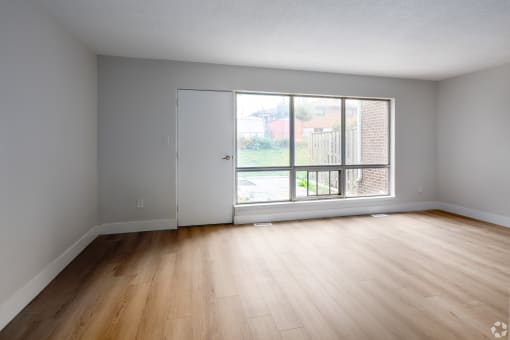 an empty living room with a large window and wooden floors