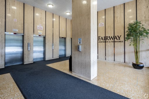 a lobby with three elevators and a plant on the floor
