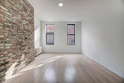 an empty living room with a brick wall and wood floors