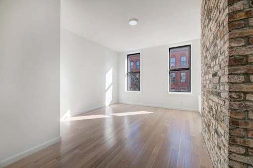 an empty living room with a brick wall and wood floors