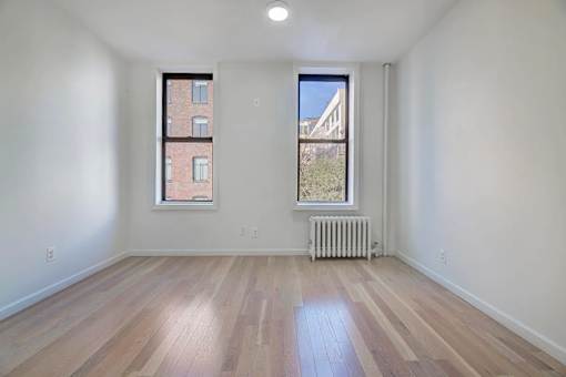 an empty living room with a radiator and two windows