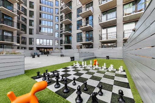 A giant chess board with pieces on a lawn in front of a building.