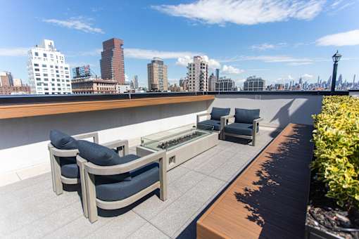 Rooftop terrace seating with fire table and city skyline at 260 Gold Apartments, Brooklyn, NY