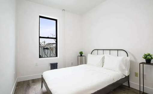 A bedroom with a large bed and a window overlooking a balcony.