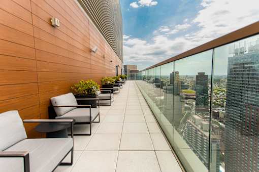 A balcony with a glass railing and a row of grey couches.