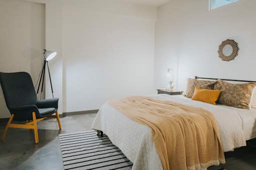 A bedroom with a bed, chair, and lamp.