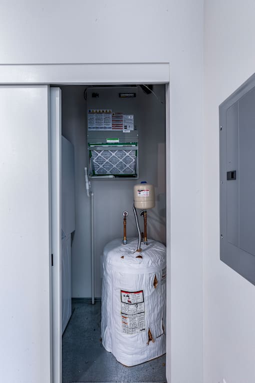 A white refrigerator with a water filter and a water heater in a small room.