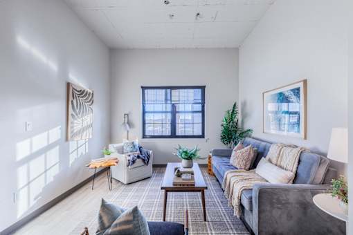 A living room with a grey couch, a white chair, a coffee table, and a window with a view of the city.