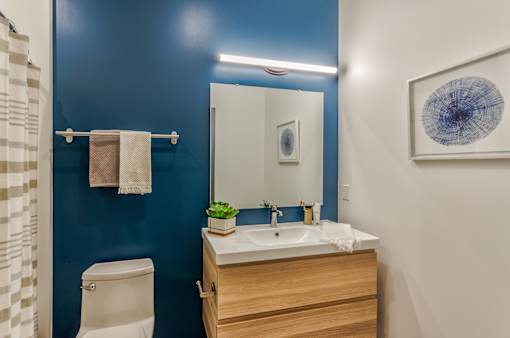 A bathroom with a white toilet, a sink with a mirror above it, and a blue wall.
