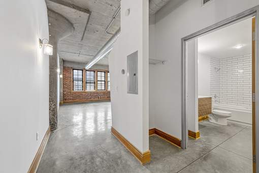 A large, empty room with a concrete floor and a brick wall.
