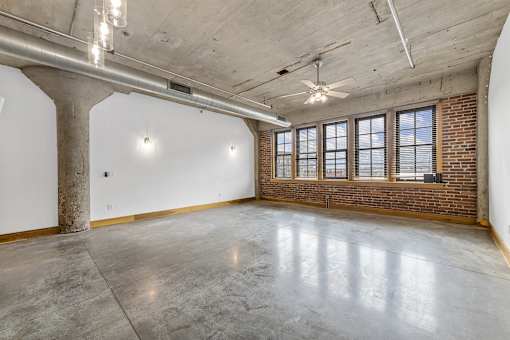 A large, empty room with a concrete floor and a brick wall.
