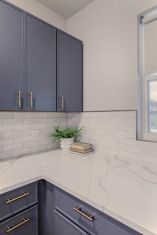 A kitchen with dark blue cabinets and a marble countertop.